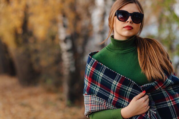 Confortable élégante jeune fille marcher au parc coloré automne à lunettes de soleil