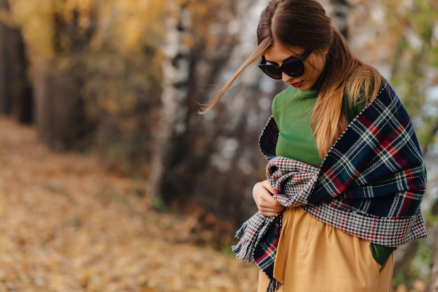Confortable élégante jeune fille marcher au parc coloré automne à lunettes de soleil
