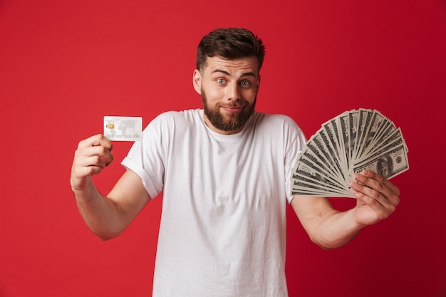 Confus jeune homme tenant de l'argent et une carte de crédit.