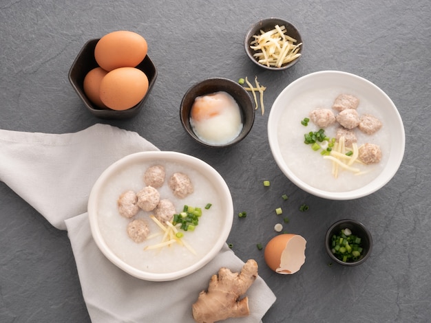 Congee de riz avec du porc haché dans un bol blanc. Bol de porridge de riz avec oeuf à la coque. Petit déjeuner asiatique