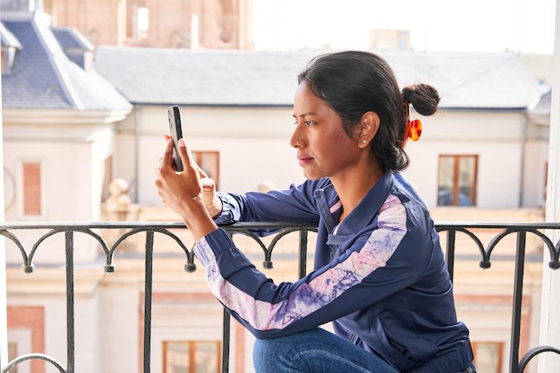 Connectée et divertissante, une jeune Indienne profite de son téléphone tout en étant assise sur le rebord de la fenêtre