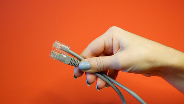 Photo connecteur réseau rj45 sur fond rouge dans des mains féminines bien entretenues