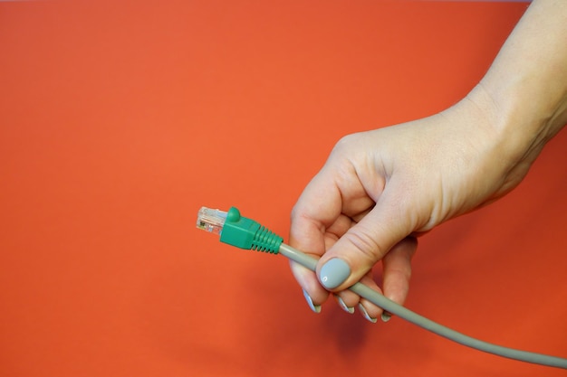 Connecteur réseau RJ45 vert sur fond rouge dans des mains féminines bien entretenues