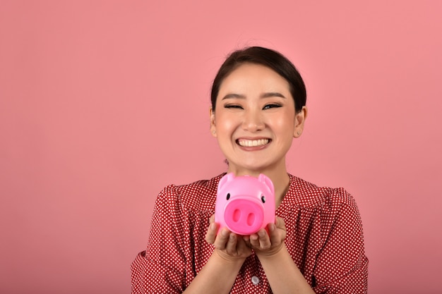 Économie d'argent, femme asiatique souriante et tenant une tirelire rose, assurance de patrimoine et de planification financière pour l'investissement.