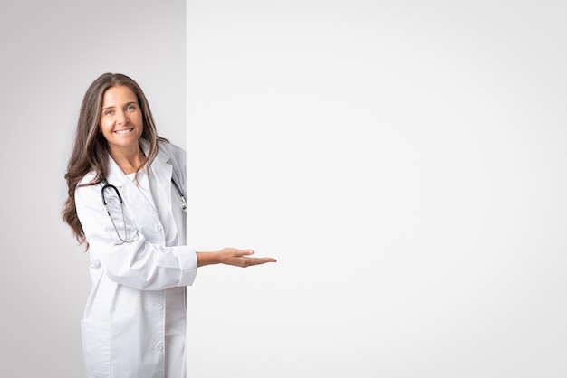 Conseil de service médical souriant femme médecin senior en manteau blanc pointant la main vers une grande bannière avec