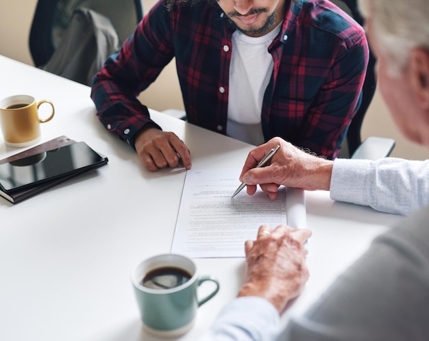 Conseiller financier aidant un jeune homme à signer un contrat d'investissement Deux hommes lors d'une réunion discutant d'un contrat à signer Comptable principal aidant un jeune homme à signer un contrat