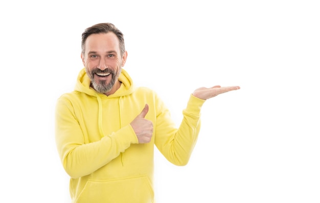 Conseiller homme en sweat à capuche jaune mec adulte publicité mâle mode sportive décontractée copie espace pouce vers le haut homme heureux mature pointant du doigt souriant mec senior présentant le produit isolé sur blanc