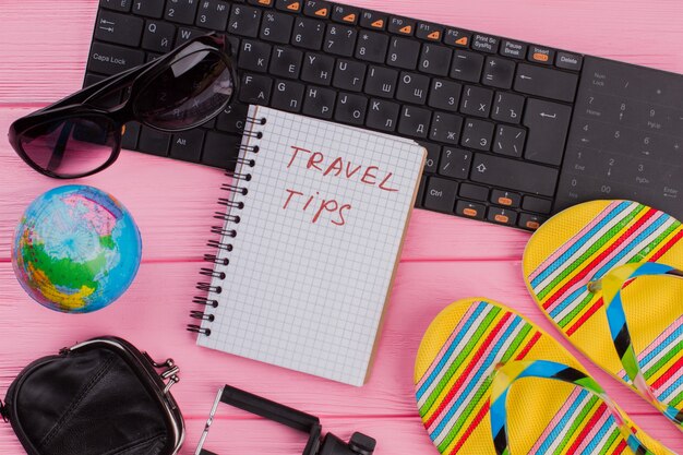 Photo conseils de voyage sur ordinateur portable avec portefeuille de lunettes d'accessoires de voyage pour femme et tongs sur fond de table rose.globe et clavier noir.