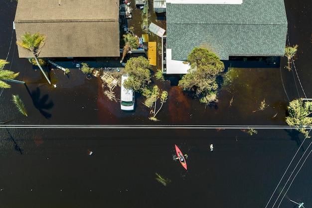 Conséquences d'une catastrophe naturelle Bateau kayak flottant sur une rue inondée entourée par l'ouragan Ian précipitations eaux d'inondation maisons dans un quartier résidentiel de Floride