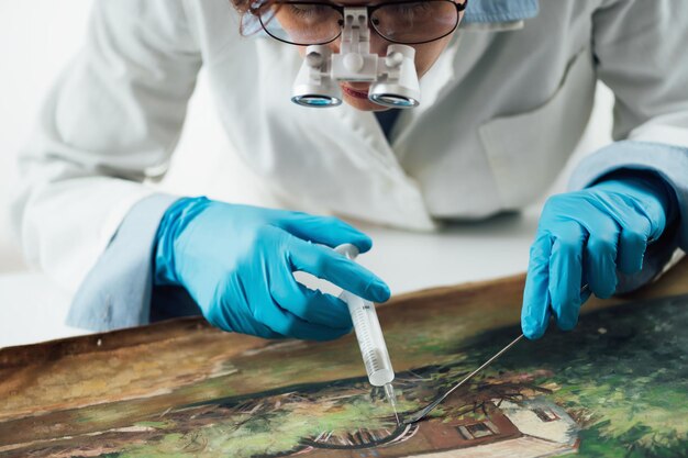 Photo une conservatrice avec des lunettes de grossissement réparant des dommages sur une toile de peinture à l'huile