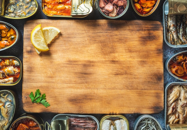 Conserver les boîtes de conserve avec différents produits de la mer ouverts sur une table sombre avec une planche en bois