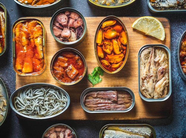 Conserver les boîtes de conserve avec différents produits de la mer ouverts sur une table sombre avec une planche en bois