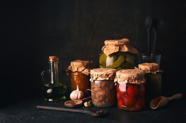 Conserves de fruits et légumes. Bocaux en verre avec des légumes et des fruits fermentés, marinés et en conserve sur une table de cuisine rustique sombre.