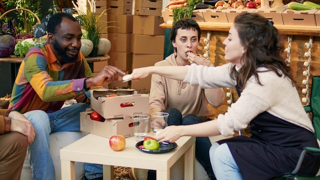 Les consommateurs s'amusent avec les exposants locaux lors du festival de tests alimentaires, en essayant des fruits et légumes cultivés localement. Clients souriants et propriétaires d'entreprise mangeant des produits et buvant du vin biologique.