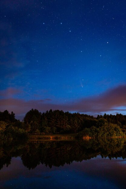 La constellation de l'ours majeur et un ciel étoilé dans les nuages et une comète au-dessus d'un lac forestier