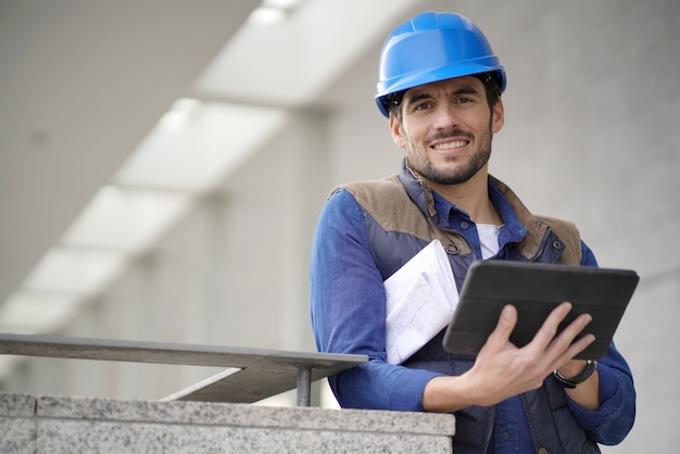 Constructeur attrayant en plein air avec tablette et plans souriant à la caméra