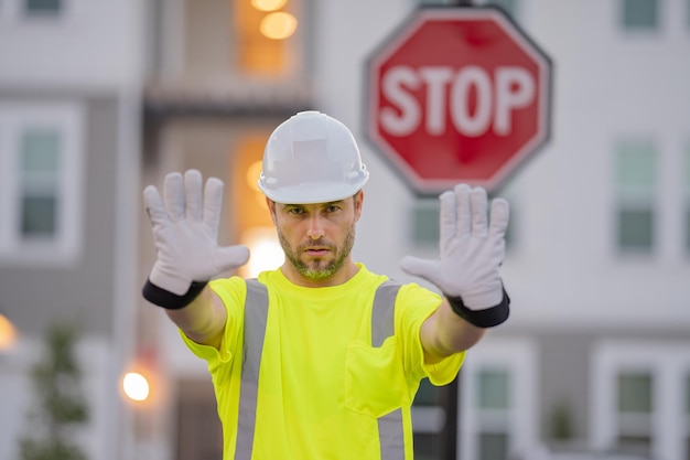 Constructeur avec geste d'arrêt aucune main dangereuse sur le concept de construction homme en casque montrant le panneau de signalisation d'arrêt