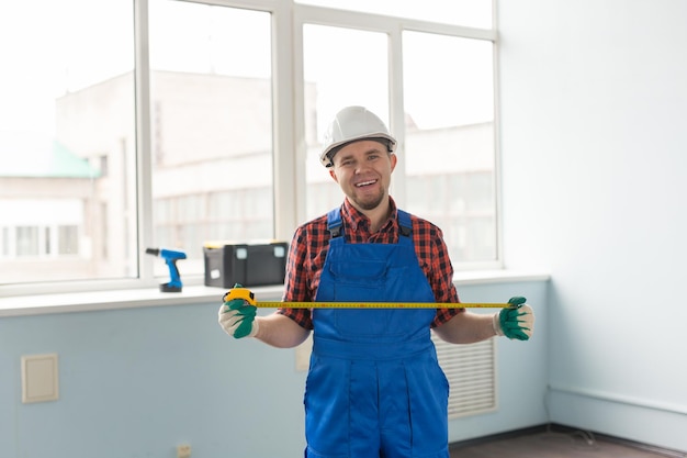 Constructeur heureux d'homme caucasien devant la fenêtre avec le ruban à mesurer