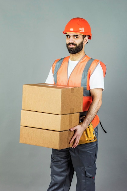 Un constructeur d'hommes dans un casque orange avec une boîte en carton dans ses mains Sur un fond gris