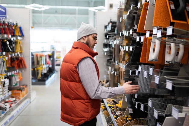 Un constructeur masculin dans une quincaillerie choisit une spatule pour enduire les murs