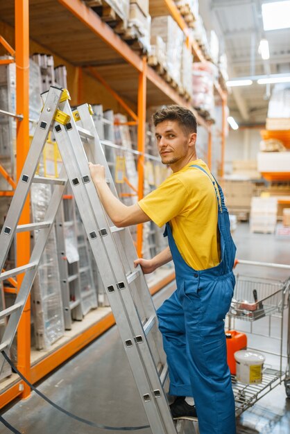 Constructeur masculin monter les escaliers en quincaillerie. Constructeur en uniforme regarde les marchandises dans la boutique de bricolage