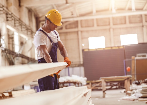 Constructeur masculin transportant la planche en bois au chantier de construction