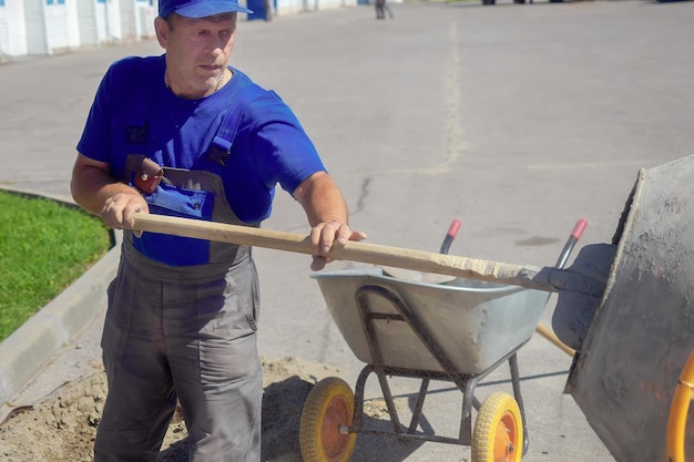 Le constructeur avec une pelle interfère avec le mortier de ciment pour la construction Un travailleur âgé travaille sur un chantier de construction le jour d'été