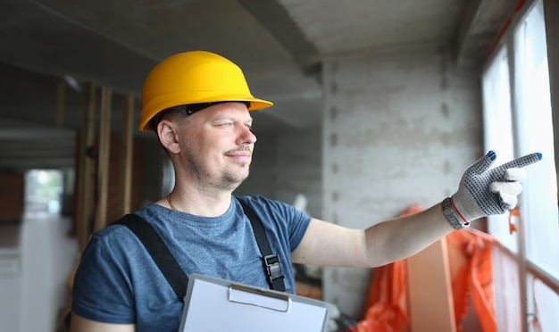 Un constructeur portant un casque regarde par la fenêtre sur le chantier de construction.
