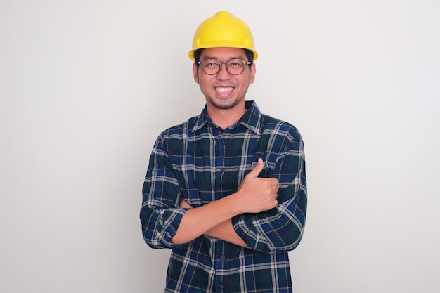 Photo un constructeur portant un chapeau dur souriant et donnant le pouce avec les bras croisés