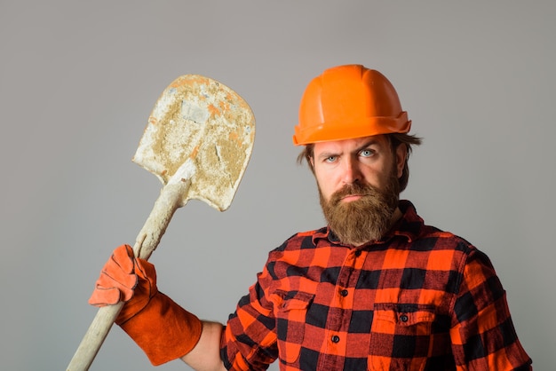 Un constructeur sérieux avec un casque avec une pelle annonce un ouvrier de réparation avec un constructeur de pelle au travail