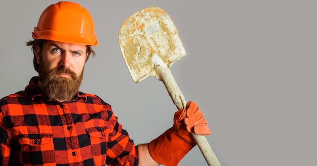 Constructeur sérieux en casque avec pelle ouvrier barbu en gants de travail et casque avec bêche