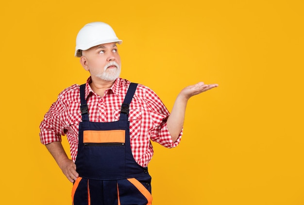 Constructeur sérieux de vieil homme dans le casque sur le fond jaune