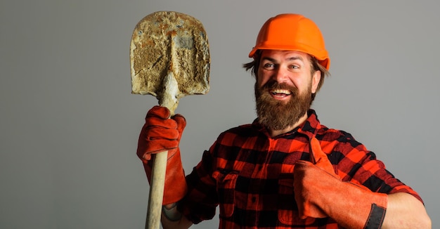Un constructeur souriant dans un casque avec une pelle montre un ouvrier dans des gants de travail avec un espace de copie de bêche