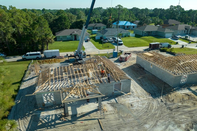 Des constructeurs professionnels et un camion grue travaillant sur la construction du toit d'une maison de banlieue inachevée avec une structure en bois dans la région rurale de la Floride.