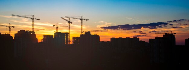 Photo construction dans les rayons du soleil couchant. silhouettes de maisons en construction et grues de ville sur un magnifique ciel coucher de soleil. image panoramique