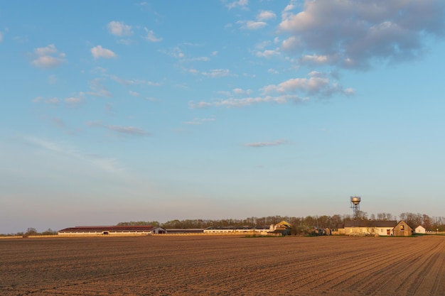 La construction d'une ferme d'élevage et d'un champ labouré au coucher du soleil Un champ agricole sur le territoire d'un complexe industriel