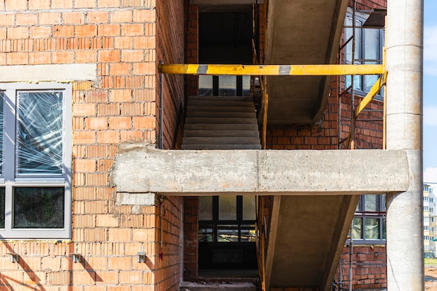 Construction d'un immeuble de plusieurs étages en brique rouge. L'utilisation d'échafaudages lors de la construction d'une maison. Construction industrielle et civile. Sécurité des chantiers.