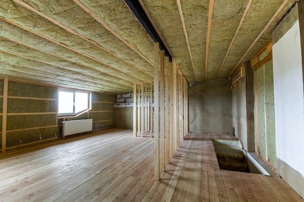 Construction et rénovation d'une grande pièce vide spacieuse et lumineuse avec parquet en chêne, murs et plafond isolés à la laine de roche, radiateurs de chauffage sous les fenêtres basses du grenier et ossature bois pour les futurs murs.