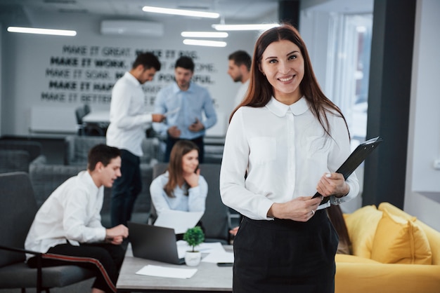 Le consultant commercial est prêt à travailler. Portrait de jeune fille se tient dans le bureau avec des employés à l'arrière-plan