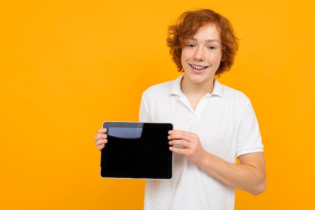 Consultant garçon frisé aux cheveux roux dans un magasin dans un T-shirt blanc montre une tablette avec une mise en page sur jaune