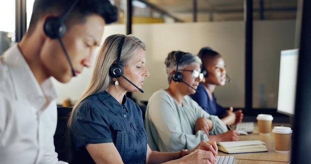 Photo consultant senior en centre d'appels femme et contactez-nous crm et parler dans l'ordinateur du service client au bureau appel téléphonique télémarketing et diversité écrit dans un ordinateur portable dans un espace de coworking et un casque