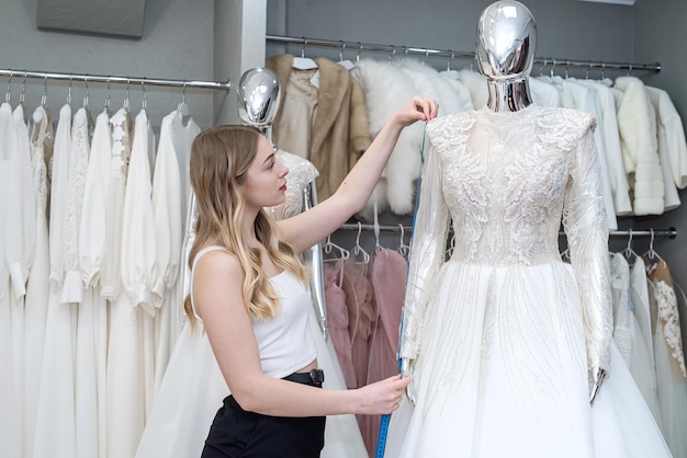 Une consultante dans un magasin mesure une robe de mariée