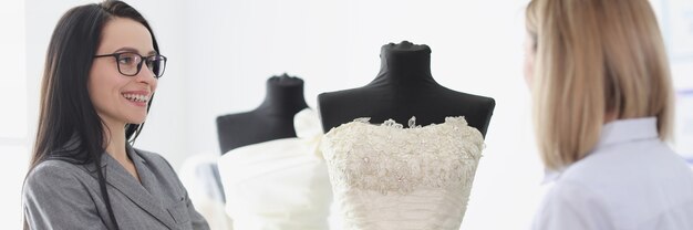 Consultante femme montrant une robe de mariée à la mariée dans un concept de couture de salon