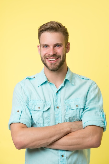 Consultante joyeuse. Homme souriant visage posant en toute confiance avec les bras croisés fond jaune. Le consultant en magasin pour homme a l'air joyeux, confiant et hospitalier. Guy avec des poils heureux de vous aider dans la boutique.