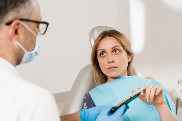 Consultation avec un dentiste sur le blanchiment des dents et montrant le guide des nuances de couleur des dents d'une patiente dans une clinique dentaire Dentisterie