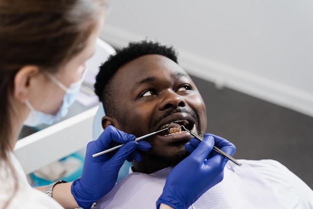 Consultation avec un dentiste à la dentisterie Traitement des dents Le dentiste examine la bouche et les dents de l'homme africain et traite les maux de dents Homme africain patient de la dentisterie