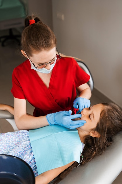 Consultation avec un dentiste pédiatrique en dentisterie Le dentiste pédiatrique examine les dents d'une petite fille pour le traitement des maux de dents Douleur dans les dents chez les enfants