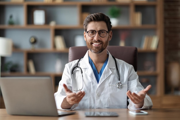 Consultation médicale beau médecin masculin assis au bureau et parler à la caméra