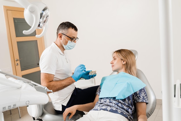 Consultation de prothèses dentaires avec un dentiste pour une femme patiente en dentisterie Un médecin dentiste montre une mâchoire artificielle en plastique avec des implants dentaires