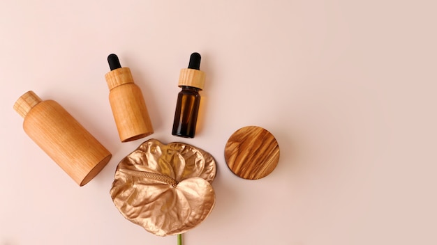 Des contenants de cosmétiques en bois se trouvent autour d'une fleur de flamant doré. Fond pastel avec espace de copie. Concept du zéro déchet, produits biologiques, grande bannière.